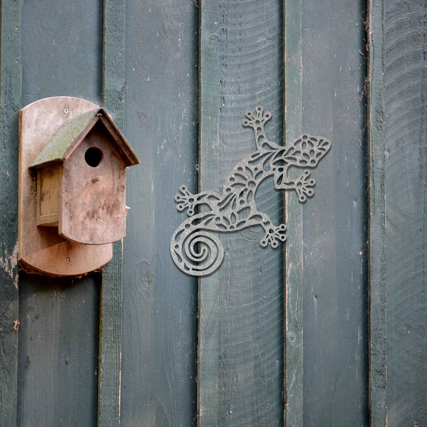 Metal garden decoration featuring a gecko design with floral and spiral cutouts, offering a playful and artistic accent to outdoor walls, seamlessly blending into rustic and natural settings.