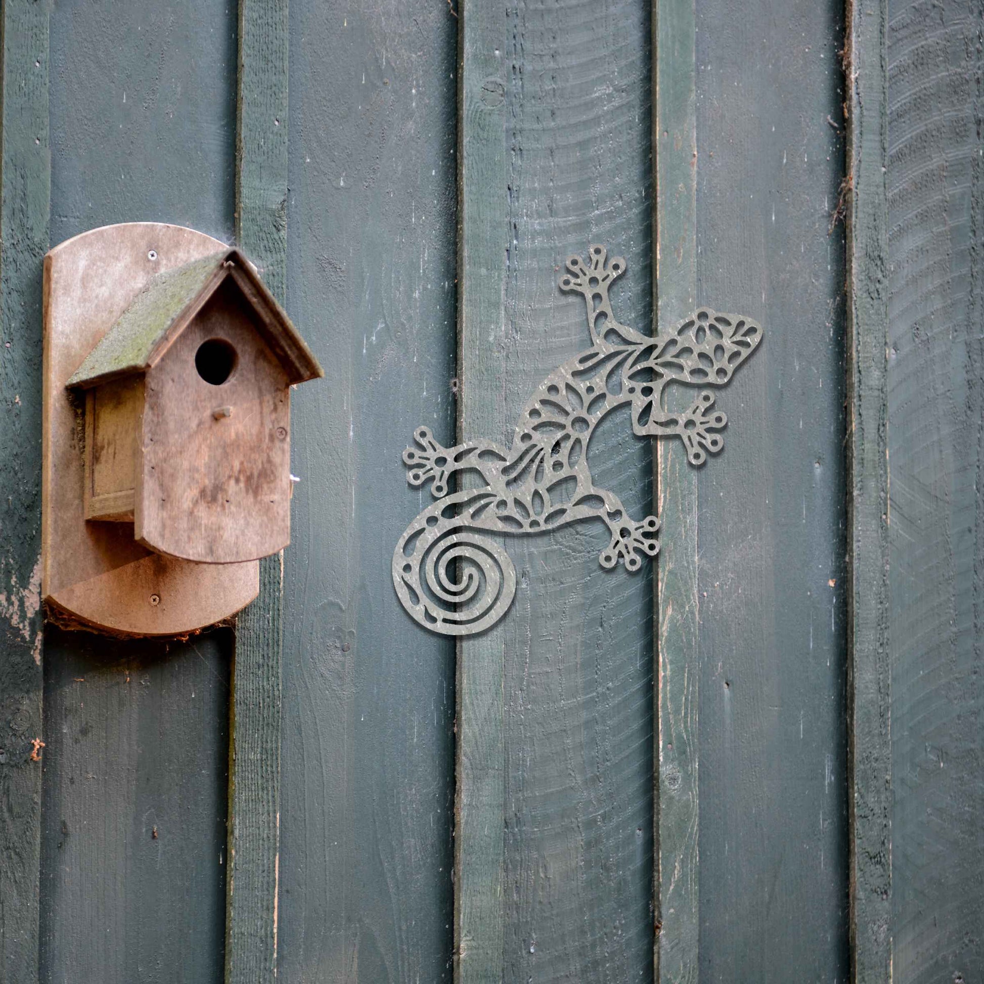Metal garden decoration featuring a gecko design with floral and spiral cutouts, offering a playful and artistic accent to outdoor walls, seamlessly blending into rustic and natural settings.
