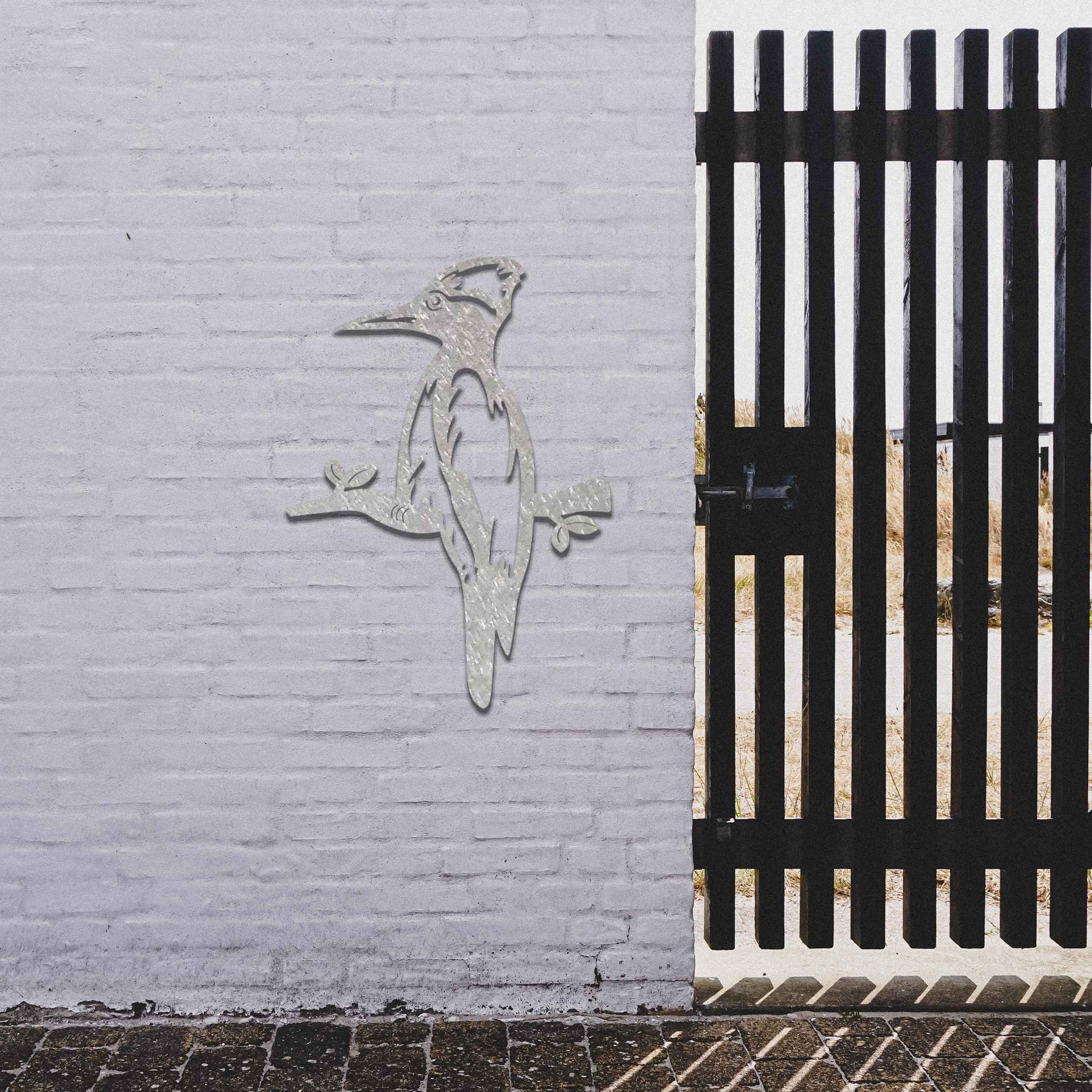 Metal garden decoration featuring a woodpecker perched on a branch, crafted with a rustic finish, adding a touch of nature-inspired charm and elegance to outdoor walls or garden settings.