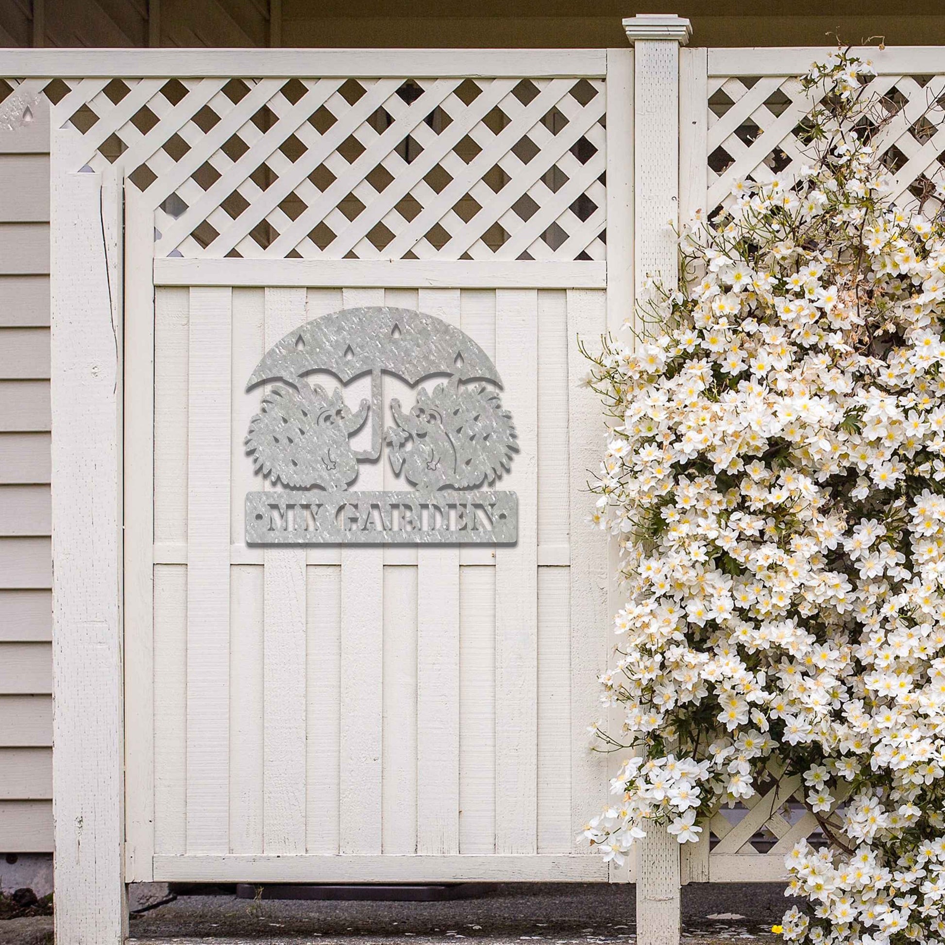 Metal garden decoration featuring two hedgehogs under an umbrella with raindrop details, accompanied by the word "Welcome," crafted with a rustic finish, adding a charming and inviting touch to outdoor spaces.