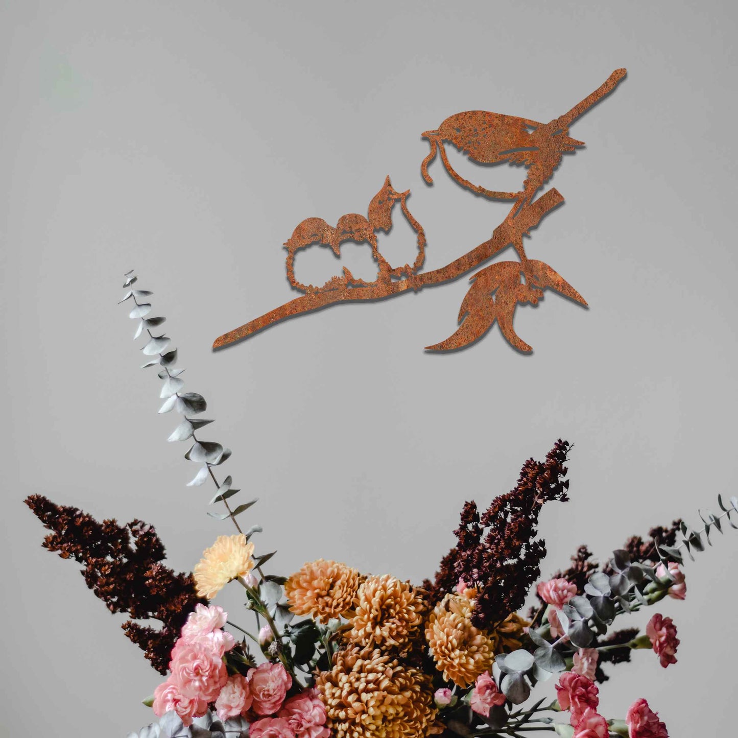 Metal wall art featuring a bird perched on a branch with two smaller birds sitting closely together, crafted in a rustic finish. This piece brings a touch of nature-inspired charm to indoor or outdoor spaces.