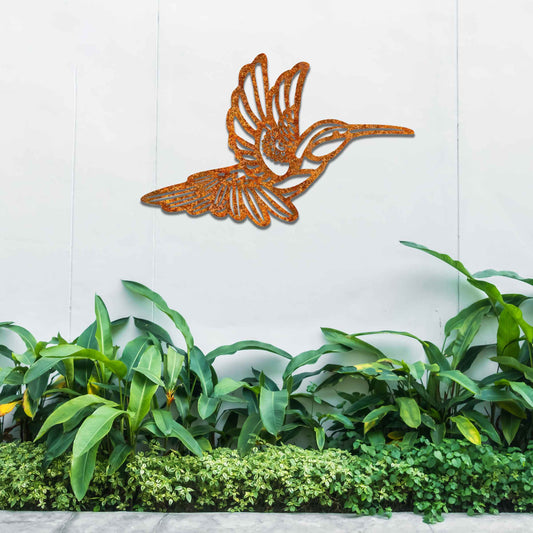 Metal garden decoration featuring a hummingbird in flight with intricate detailing, showcasing a rustic finish that adds a natural and artistic charm to outdoor walls or garden settings.