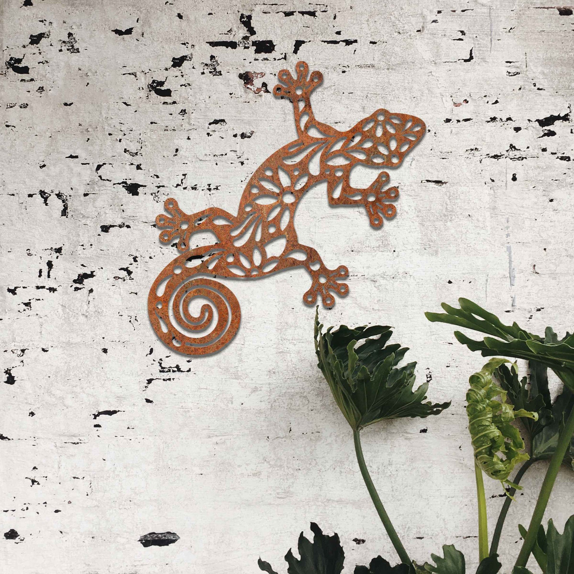 Metal garden decoration featuring a gecko design with floral and spiral cutouts, offering a playful and artistic accent to outdoor walls, seamlessly blending into rustic and natural settings.