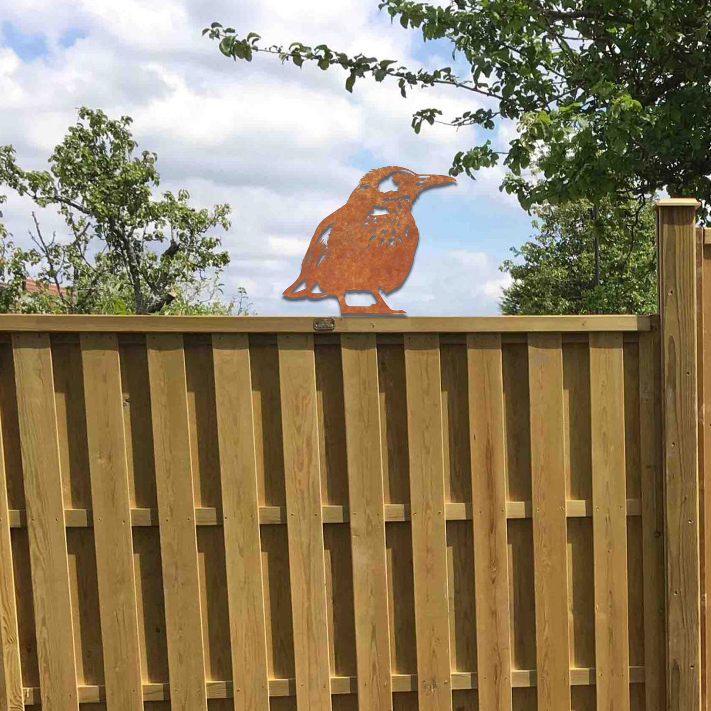 Metal wall art of a bird perched on a wooden fence post, featuring detailed wing and feather patterns. The bird is in a relaxed pose, surrounded by sunflowers, showcasing nature's beauty.