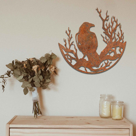 Metal wall decoration featuring a crow perched on detailed tree branches within a circular frame, crafted with intricate cutouts and a rustic finish, adding a bold and artistic touch to indoor or outdoor spaces.
