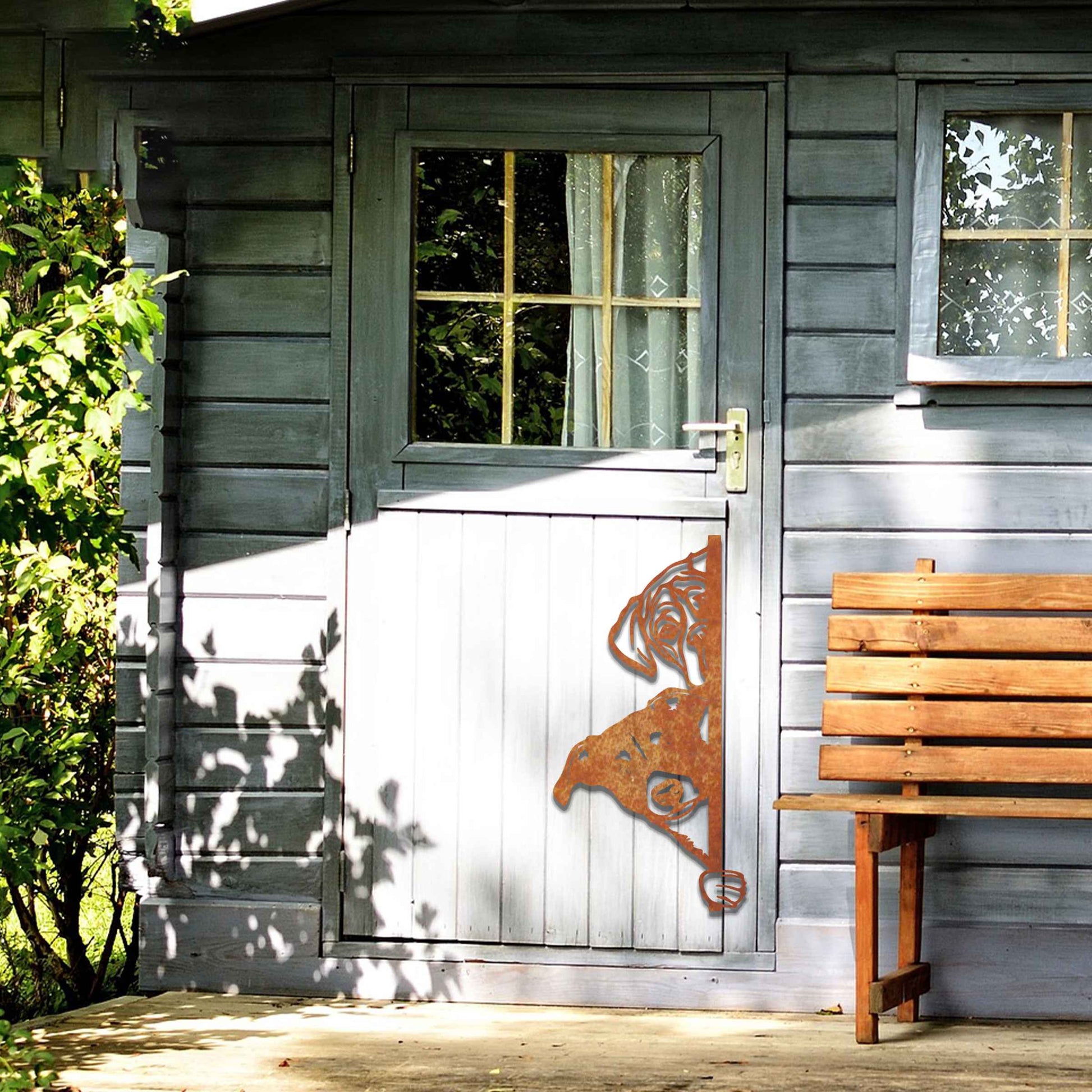 This image features a playful dog peeking through a gate, captured in a rusted finish. Its curious expression brings a whimsical touch to the surroundings, creating an inviting, charming atmosphere for any garden or outdoor space.