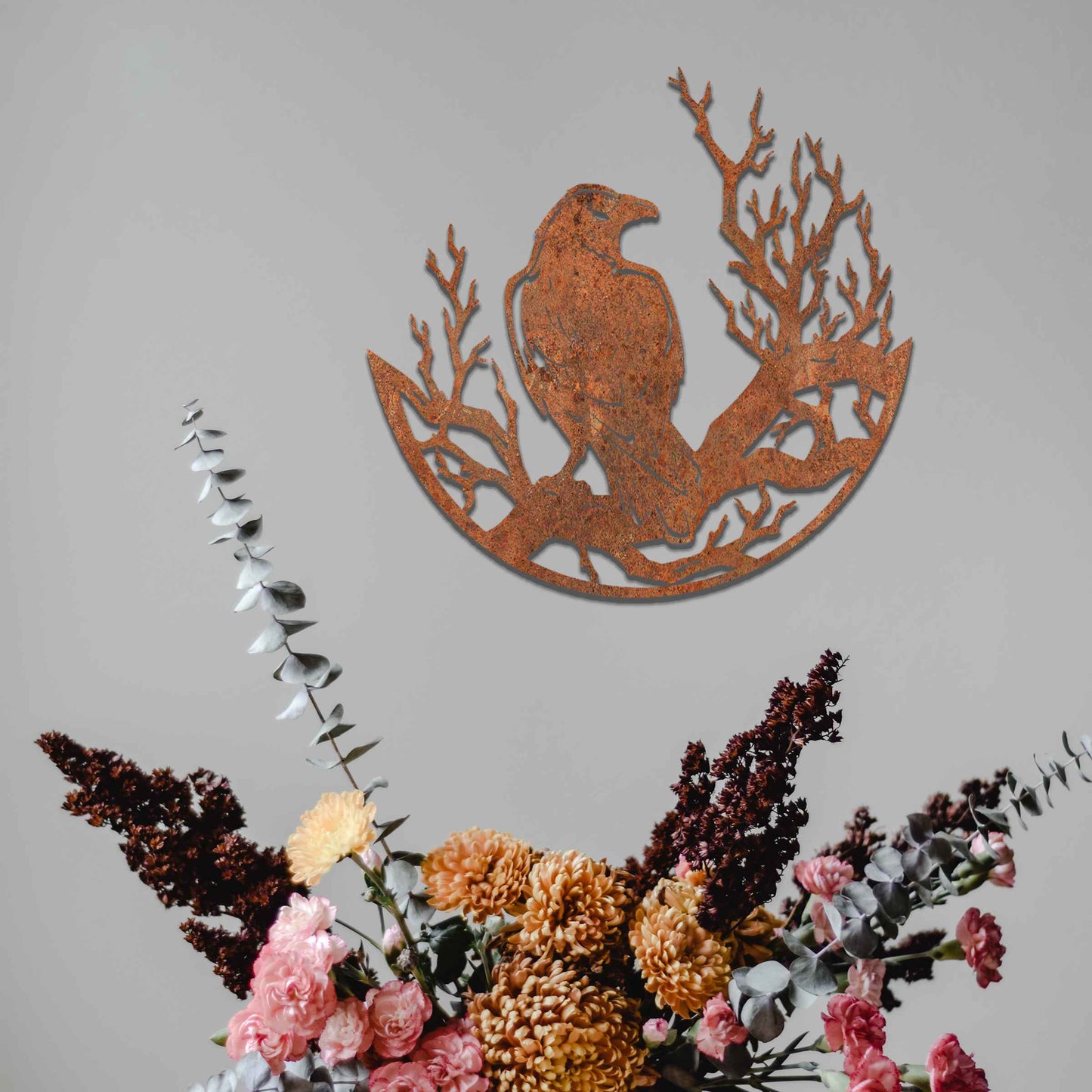 Metal wall decoration featuring a crow perched on detailed tree branches within a circular frame, crafted with intricate cutouts and a rustic finish, adding a bold and artistic touch to indoor or outdoor spaces.