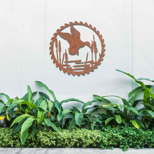 Metal garden decoration featuring a duck in flight over a pond surrounded by cattails, enclosed within a circular saw blade design, combining rustic charm and outdoor-inspired artistry to enhance garden or wall decor.