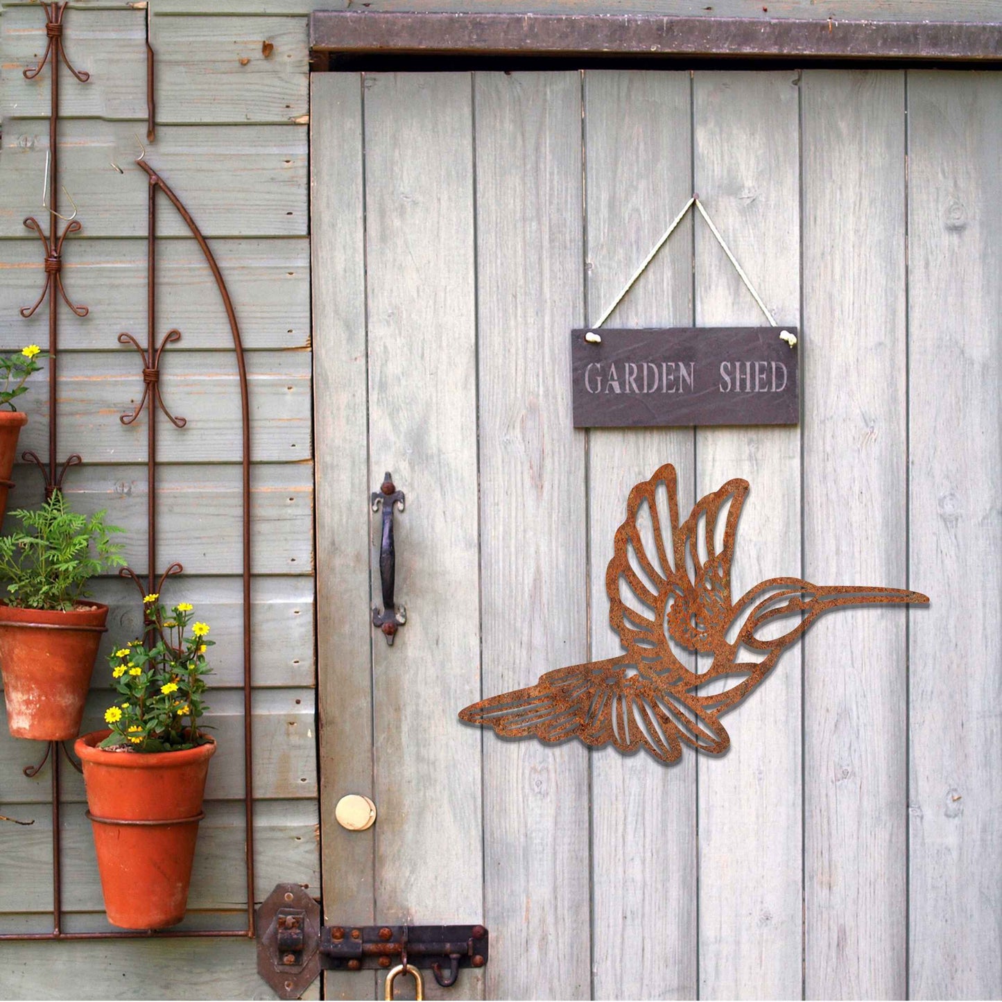 Metal garden decoration featuring a hummingbird in flight with intricate detailing, showcasing a rustic finish that adds a natural and artistic charm to outdoor walls or garden settings.