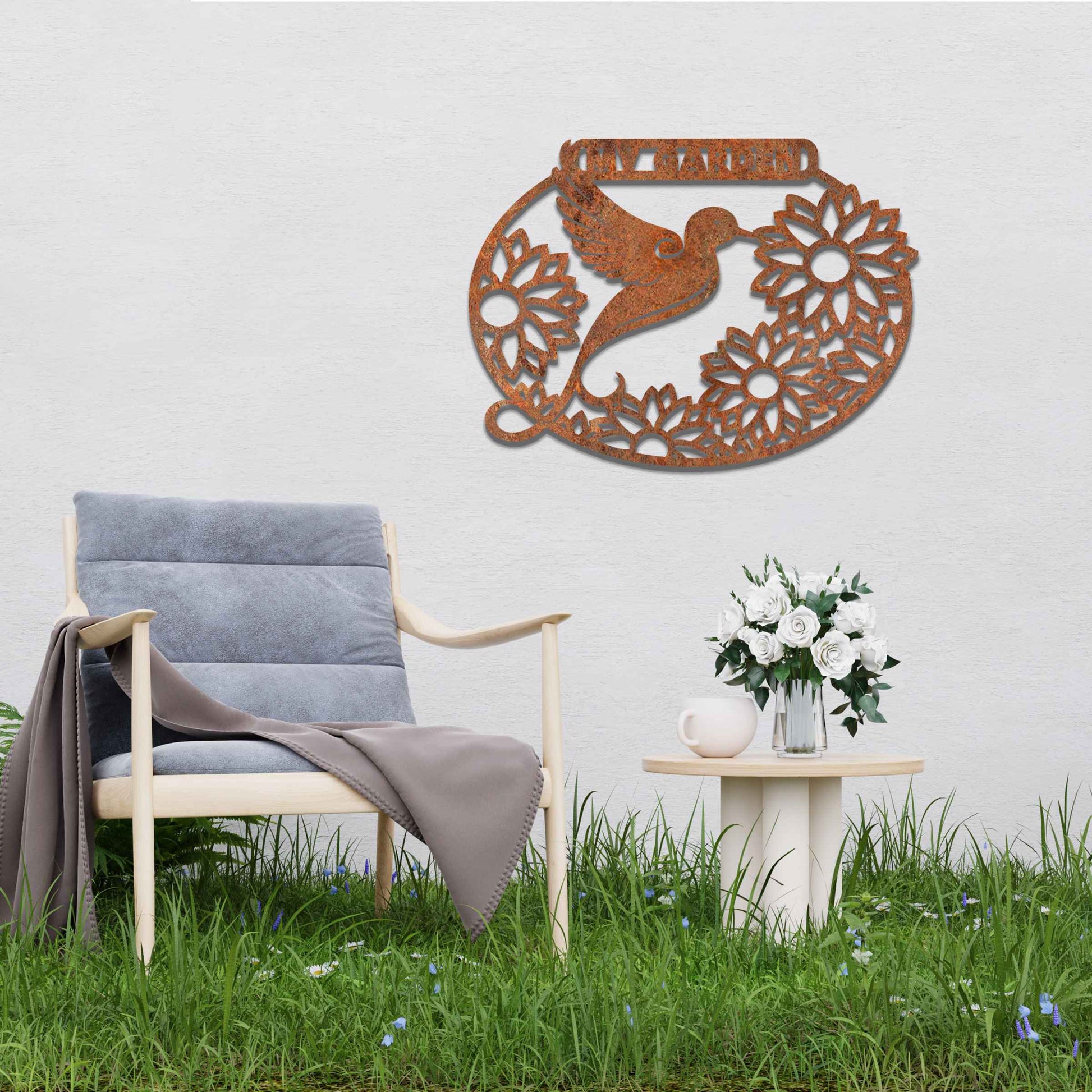 Metal garden decoration featuring a hummingbird surrounded by blooming sunflowers within an oval frame, inscribed with "My Garden," adding a personalised and nature-inspired charm to outdoor walls or fences.