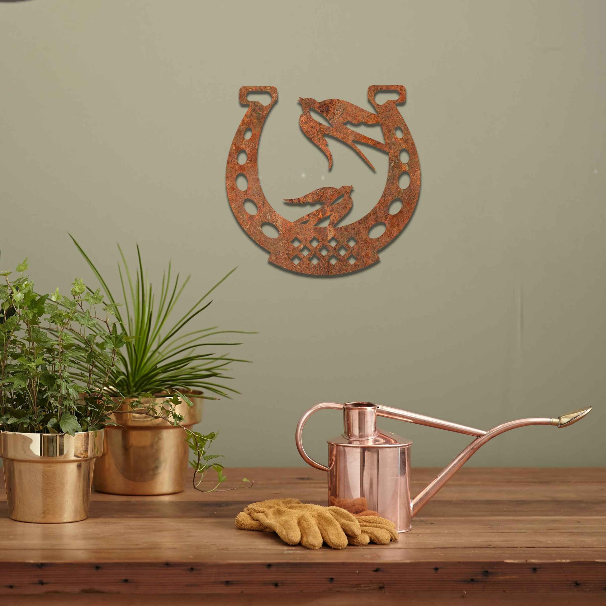 Metal garden decoration featuring two swallows perched within a horseshoe design, crafted with intricate detailing to symbolise luck and harmony, adding a rustic and charming touch to outdoor walls or fences.