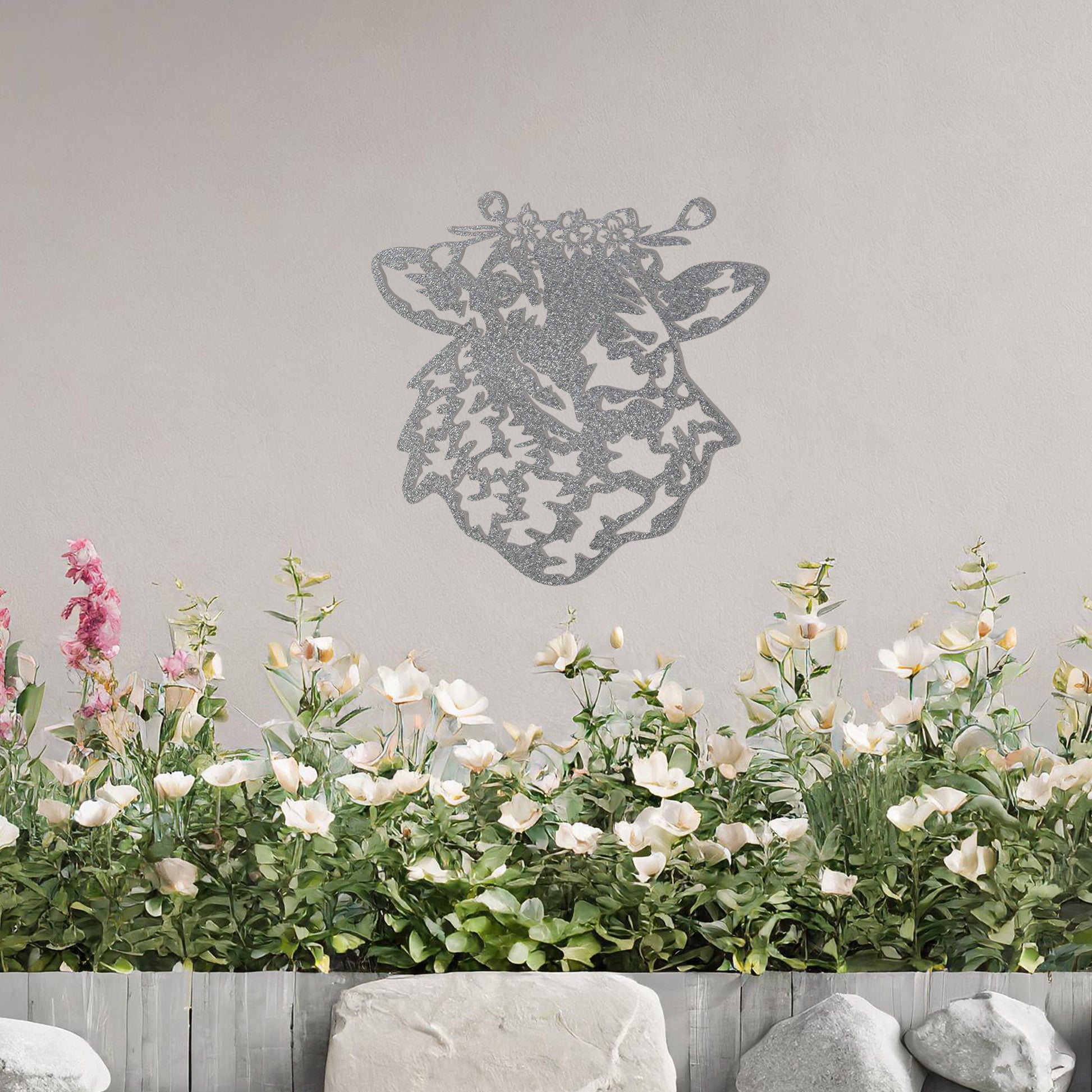 A metal wall art piece depicting a sheep adorned with a floral crown, exuding rustic charm and elegance. This intricate design brings a touch of countryside serenity to any modern or natural setting, complemented by its leafy surroundings.
