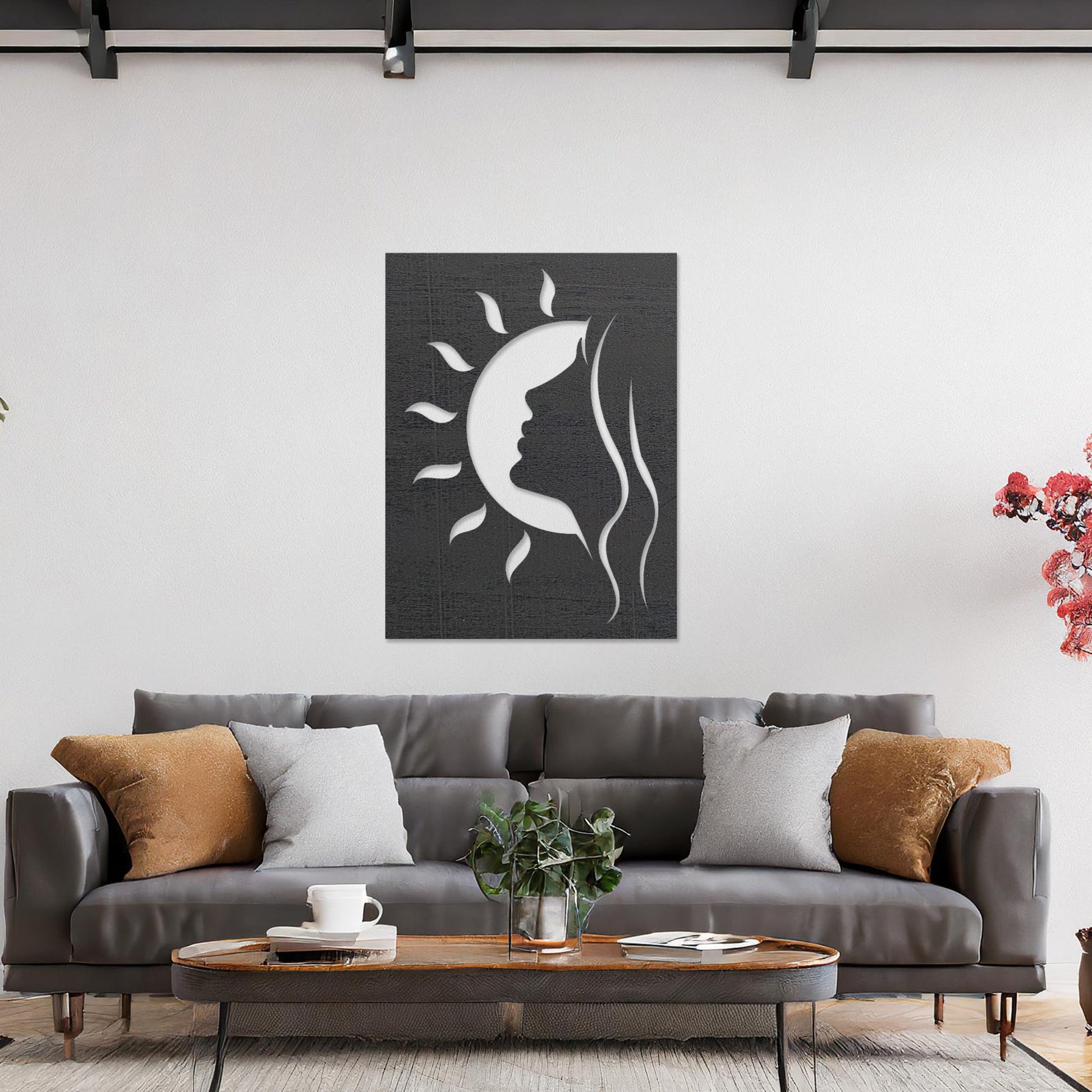 A rectangular wall art piece featuring a silhouette of a face intertwined with a crescent moon and radiating sun rays. The artwork is displayed on a neutral wall in a modern living room