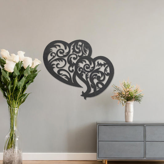 Wooden wall art design featuring two interlocking hearts with intricate swirling patterns, placed on a neutral wall within modern room decor. The design combines elegance and romance with its flowing shapes and fine details.