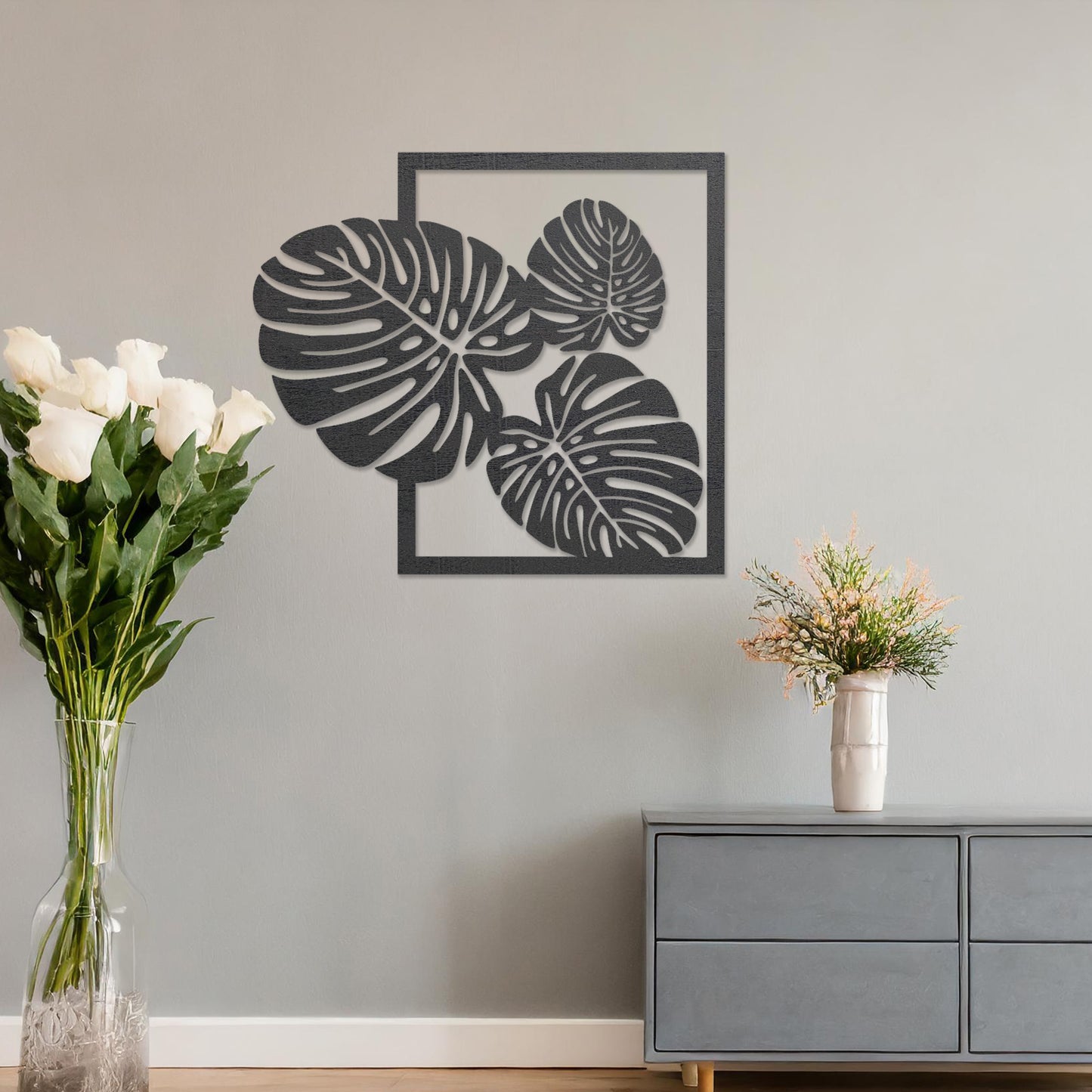 Wall art featuring a botanical design of overlapping monstera leaves framed within a rectangular border. The piece is displayed on a neutral wall within modern room decor, enhancing the natural and elegant aesthetic.