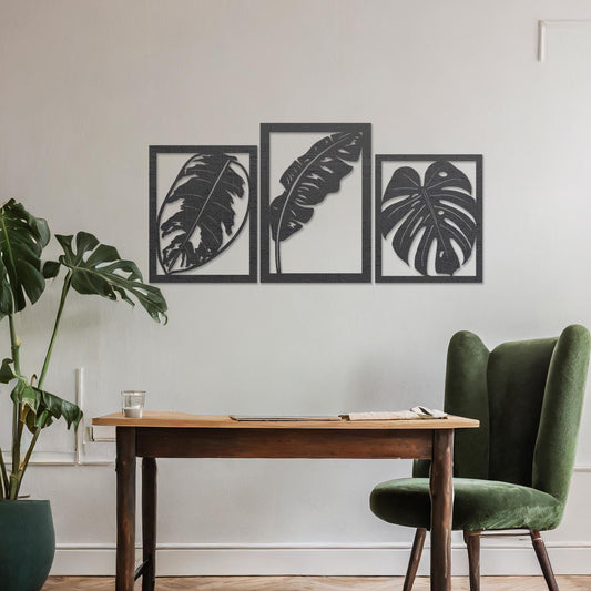 A three-piece wall art set featuring artistic depictions of tropical leaves, including monstera and banana leaves, framed in a rectangular layout. The artwork is displayed on a neutral wall in a modern room