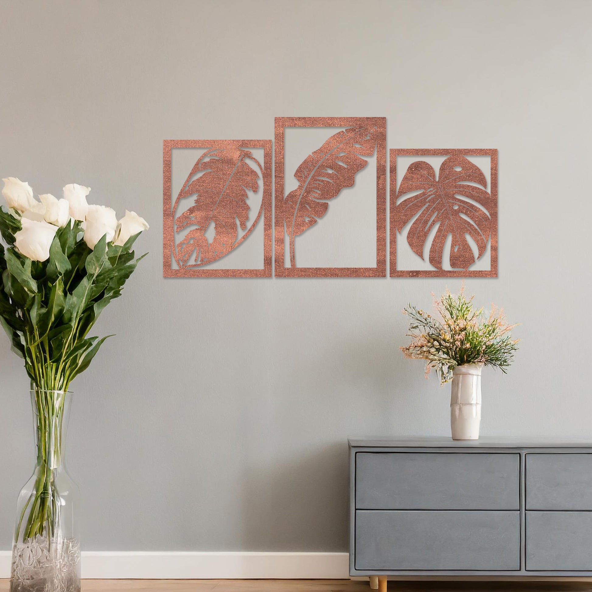 A three-piece wall art set featuring artistic depictions of tropical leaves, including monstera and banana leaves, framed in a rectangular layout. The artwork is displayed on a neutral wall in a modern room