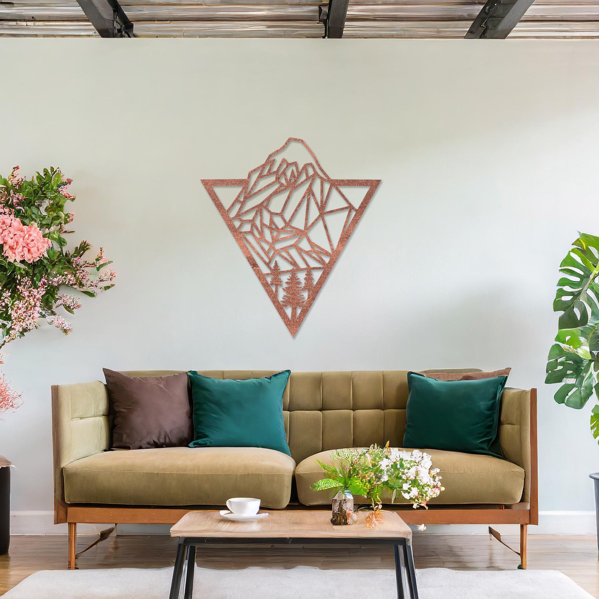 Triangular wall art featuring a geometric mountain landscape design with trees at the base, evoking nature and adventure. The piece is displayed on a neutral wall in a modern living room with a stylish sofa and contemporary decor.