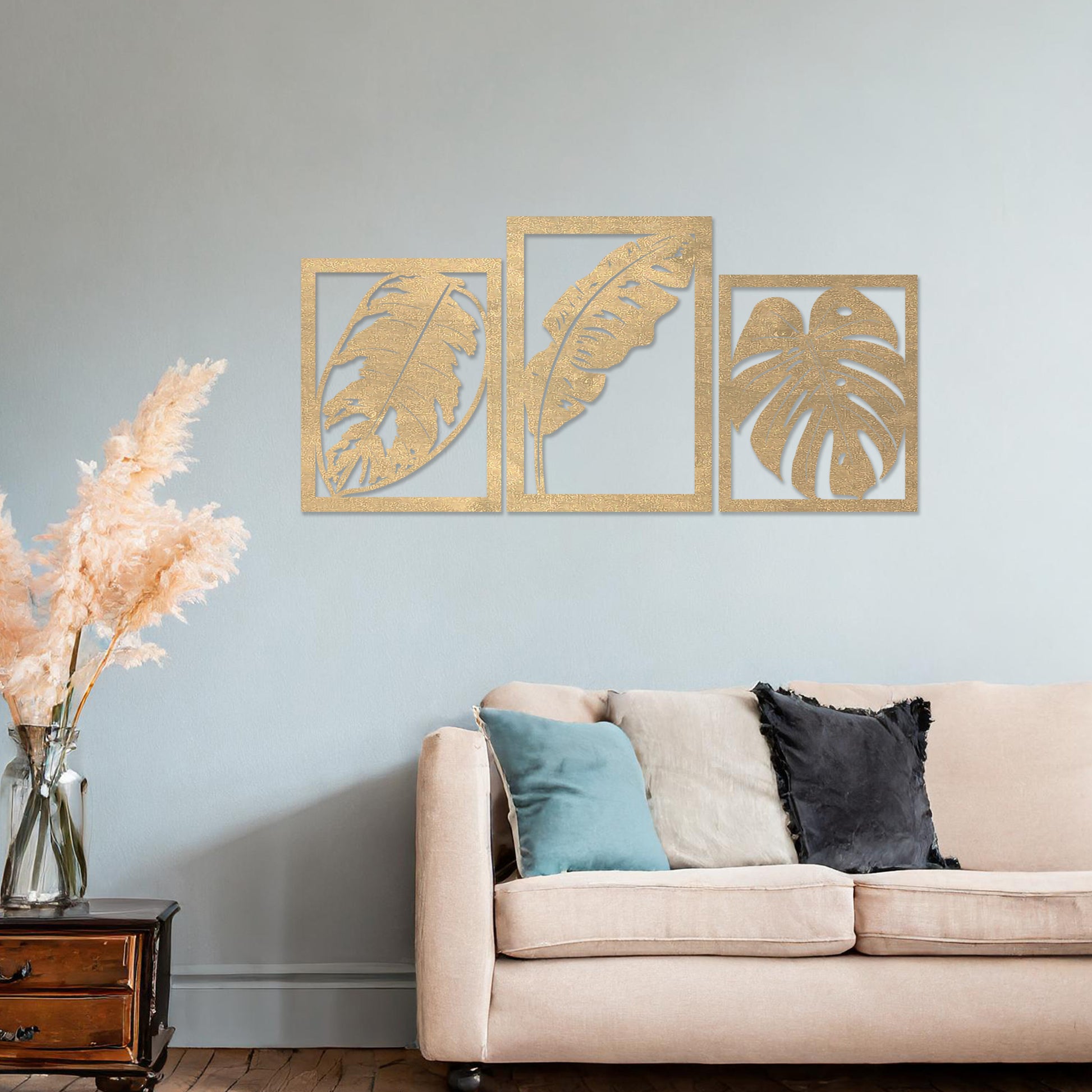 A three-piece wall art set featuring artistic depictions of tropical leaves, including monstera and banana leaves, framed in a rectangular layout. The artwork is displayed on a neutral wall in a modern room