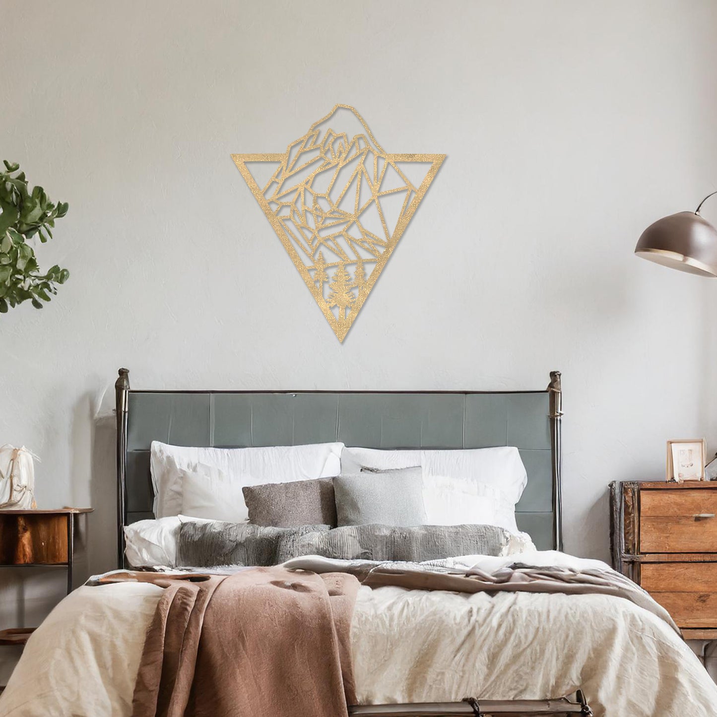 Triangular wall art featuring a geometric mountain landscape design with trees at the base, evoking nature and adventure. The piece is displayed on a neutral wall in a modern living room with a stylish sofa and contemporary decor.