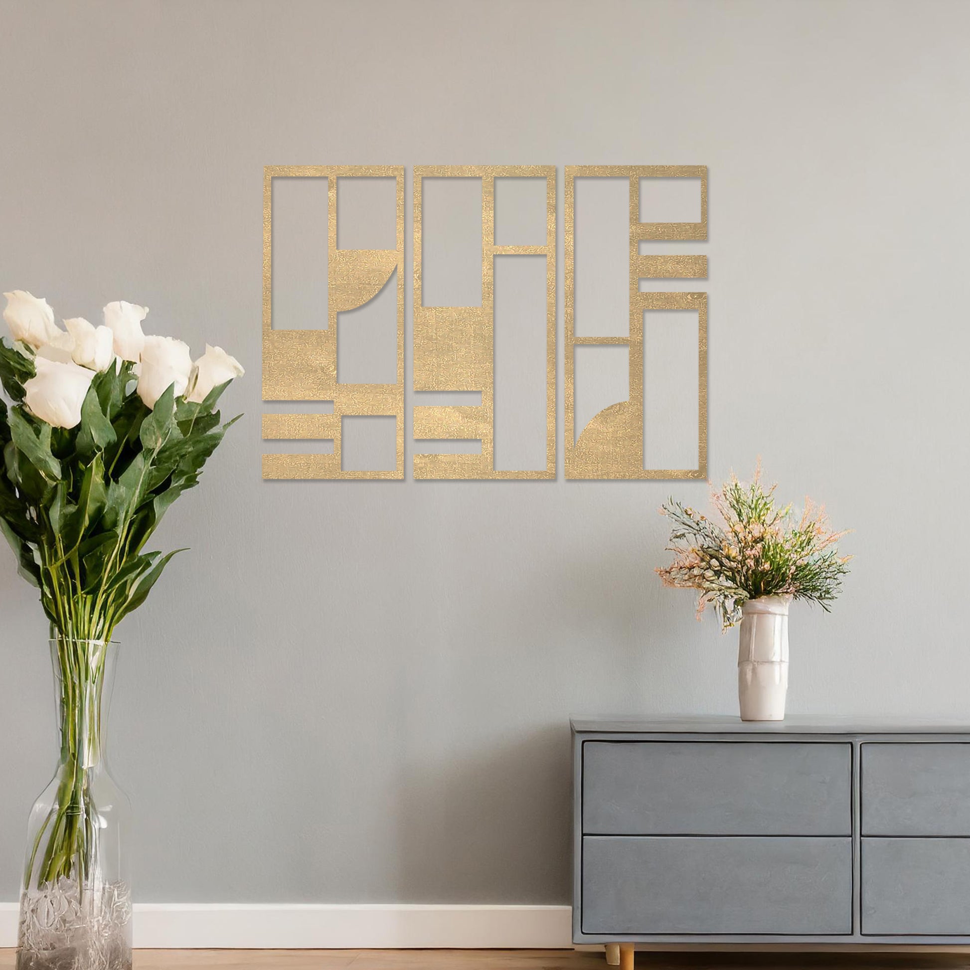 This image displays a modern, abstract triptych wall art piece featuring geometric patterns in dark tones. The artwork is placed above a simple desk setup with a plant and a chair, providing a stylish and minimalistic atmosphere suitable for a contemporary workspace. 