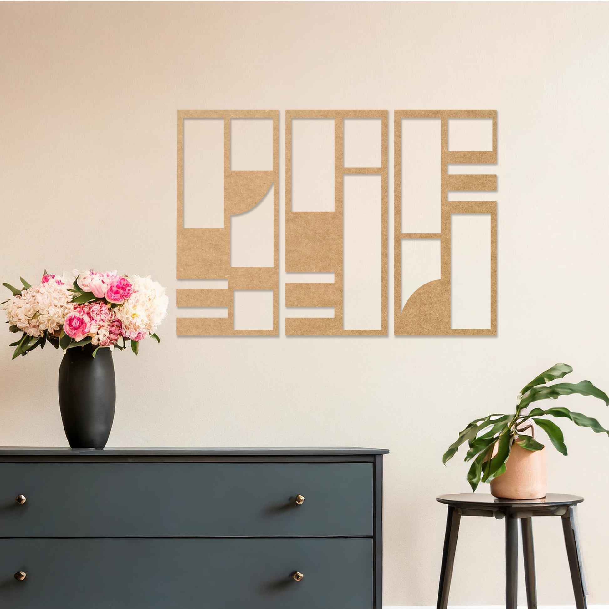This image displays a modern, abstract triptych wall art piece featuring geometric patterns in dark tones. The artwork is placed above a simple desk setup with a plant and a chair, providing a stylish and minimalistic atmosphere suitable for a contemporary workspace. 