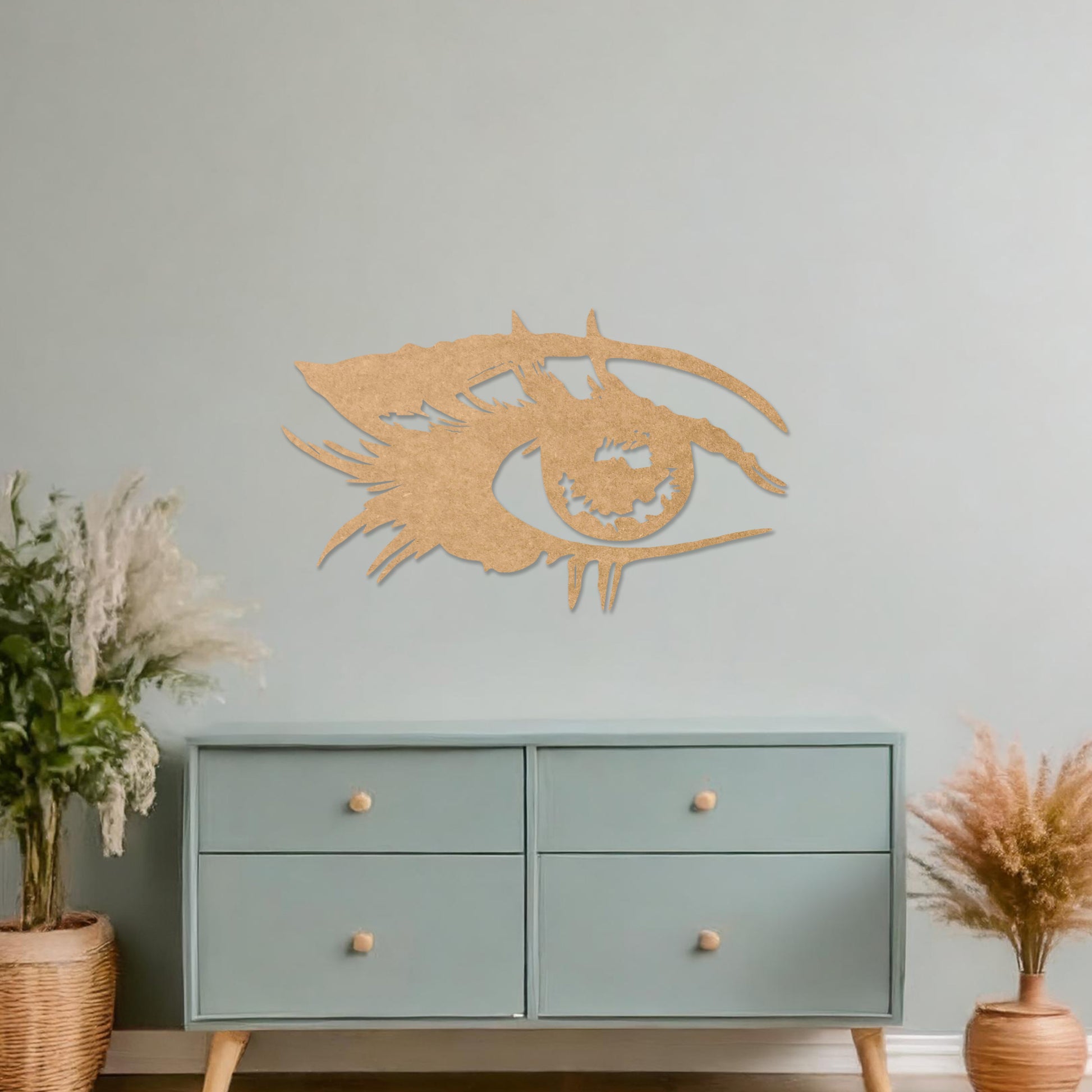 Wooden wall art featuring a stylised eye design with intricate detailing of lashes and bold lines. The artwork is displayed on a neutral wall within modern room decor, emphasising its artistic and striking pattern.