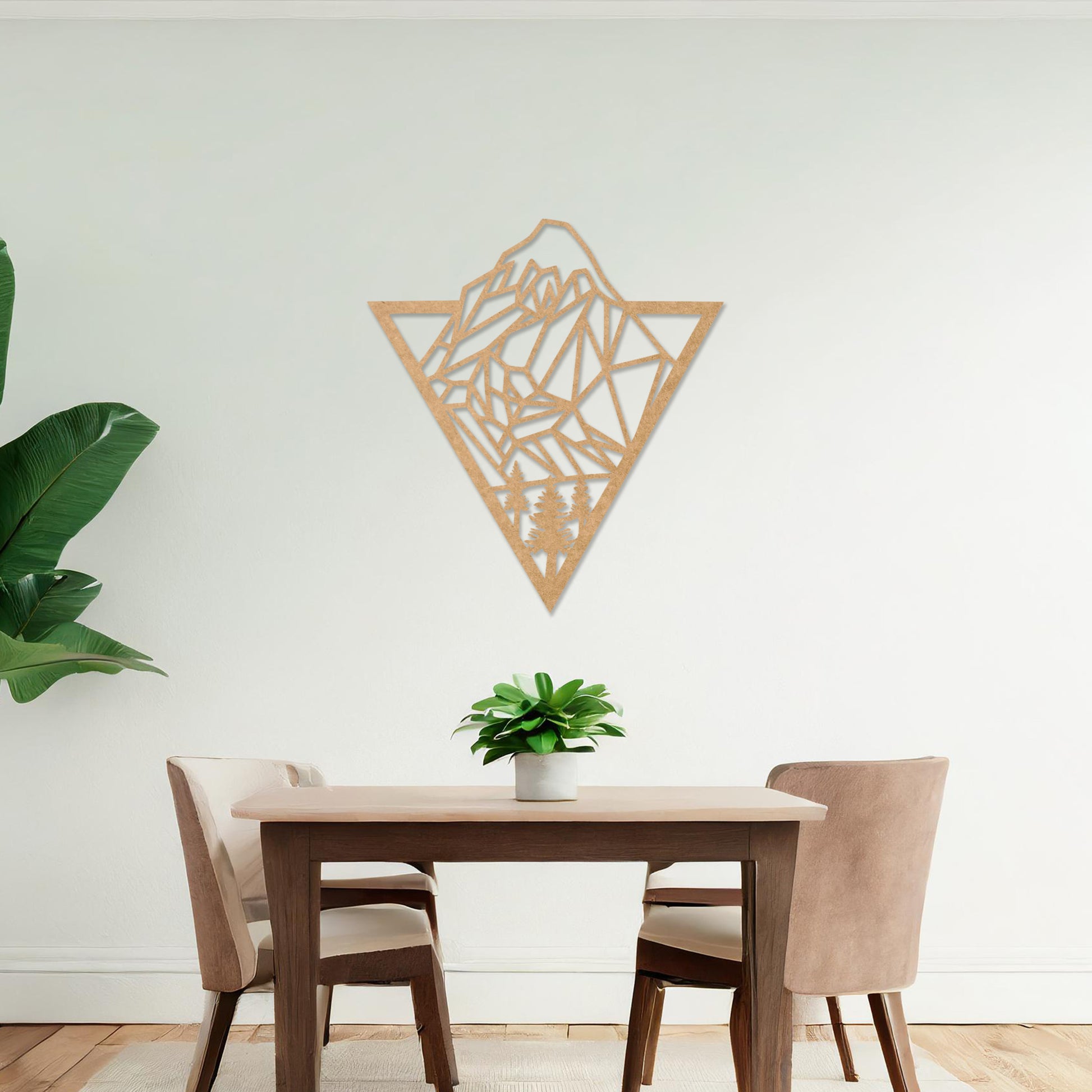 Triangular wall art featuring a geometric mountain landscape design with trees at the base, evoking nature and adventure. The piece is displayed on a neutral wall in a modern living room with a stylish sofa and contemporary decor.