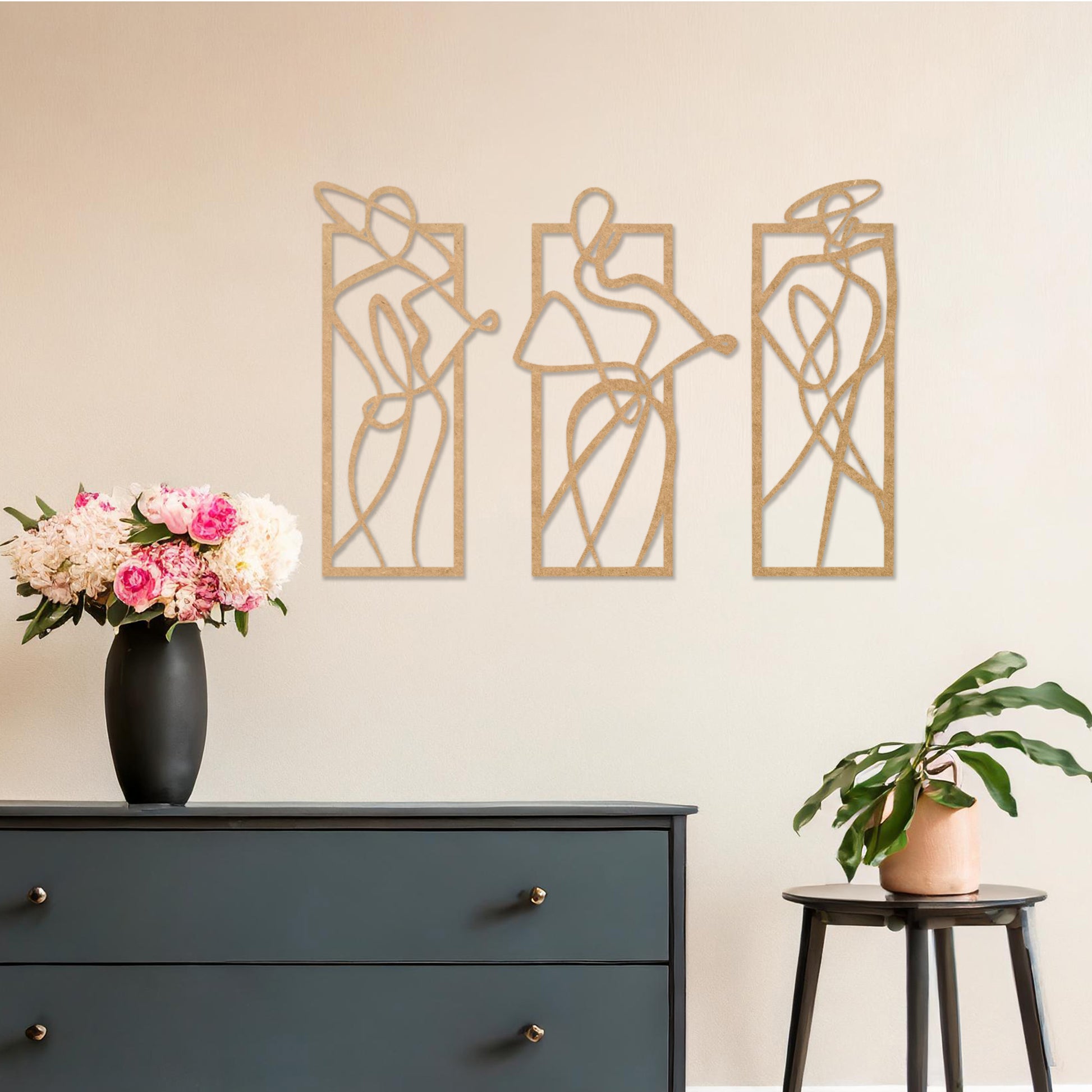 Wooden wall art design featuring three abstract figures in flowing lines, each in its own rectangular frame, placed on a neutral wall with modern room decor. The design evokes movement and elegance through minimalistic, artistic shapes.