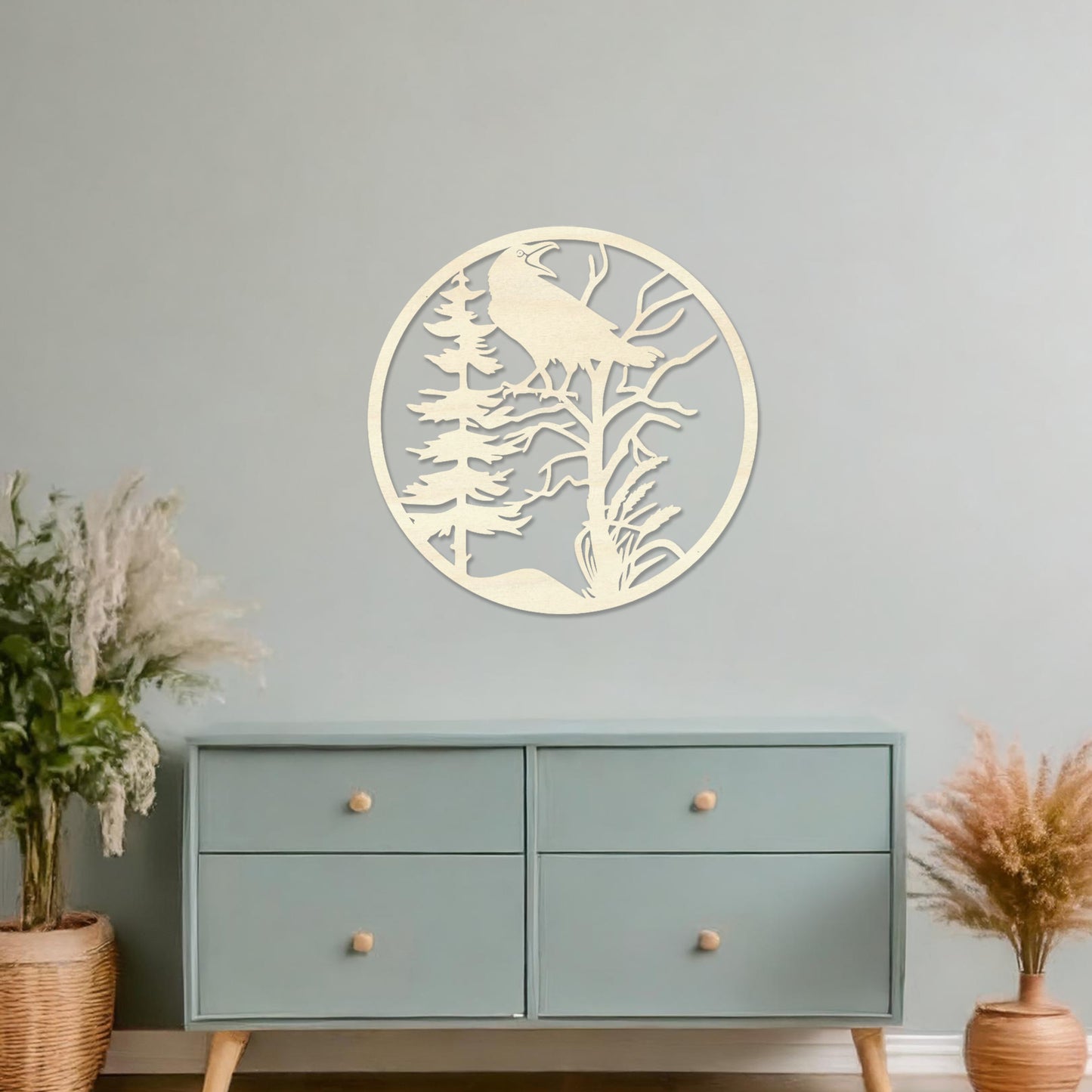 Wooden wall art featuring a circular design with a silhouette of a bird perched on a tree surrounded by natural elements. The artwork is displayed on a neutral wall within modern room decor, highlighting its rustic and nature-inspired design.