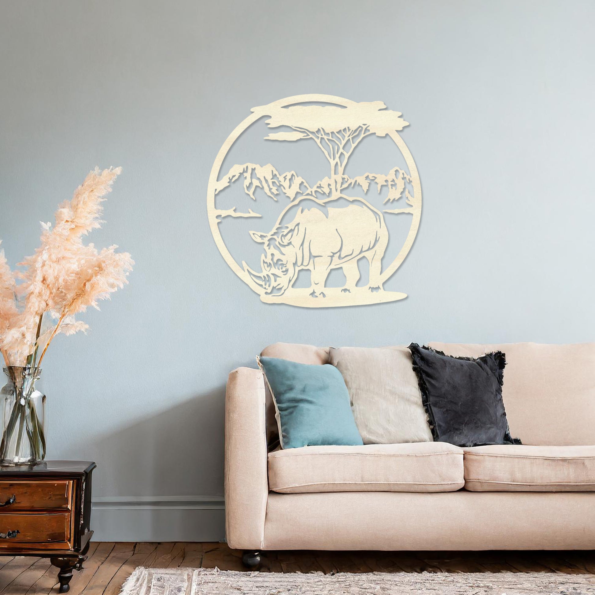 Wooden wall art design featuring a rhinoceros beneath a tree with a mountain backdrop, framed in a circular shape, placed on a neutral wall within modern room decor. The design captures the majesty of wildlife in a serene landscape.