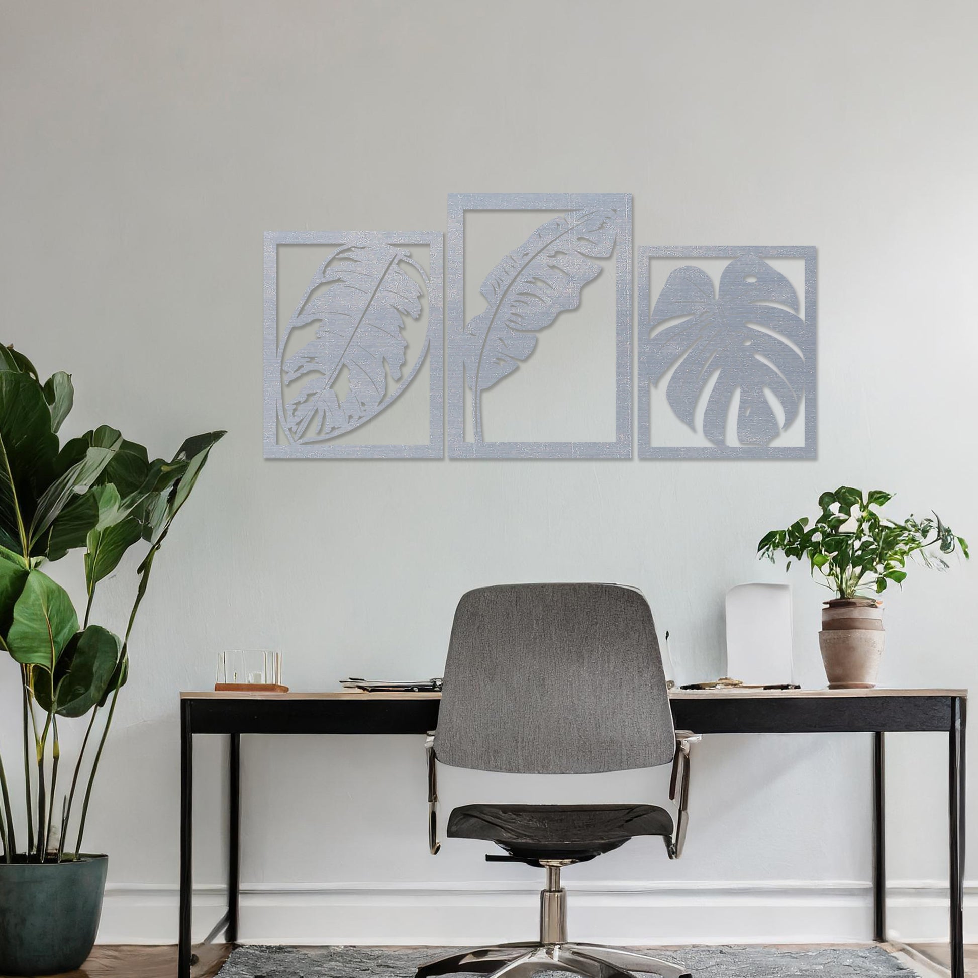 A three-piece wall art set featuring artistic depictions of tropical leaves, including monstera and banana leaves, framed in a rectangular layout. The artwork is displayed on a neutral wall in a modern room