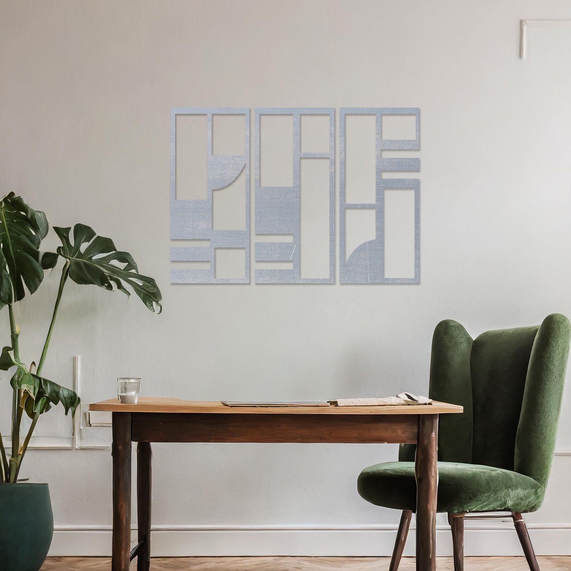 This image displays a modern, abstract triptych wall art piece featuring geometric patterns in dark tones. The artwork is placed above a simple desk setup with a plant and a chair, providing a stylish and minimalistic atmosphere suitable for a contemporary workspace. 