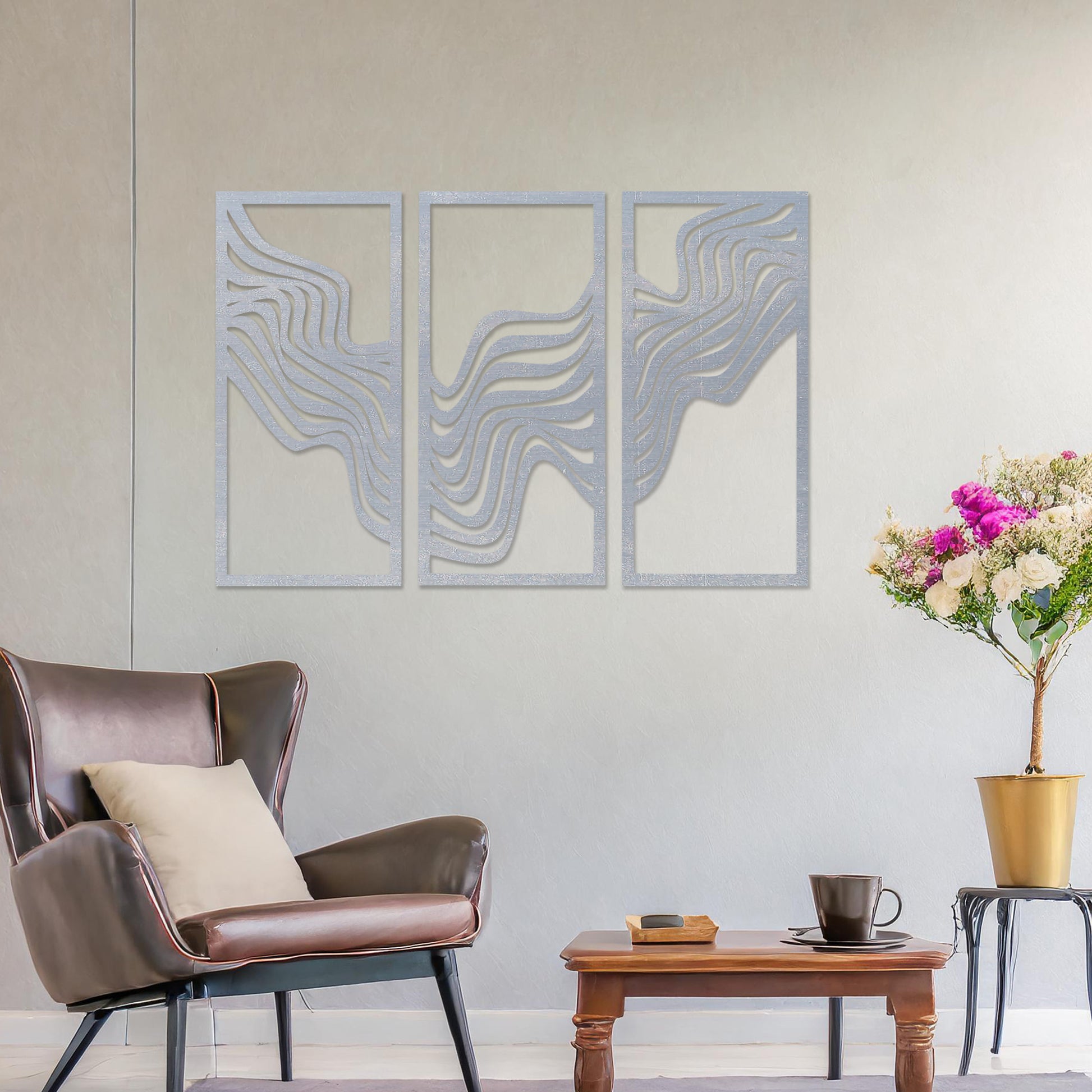 This image displays a modern triptych wall art design featuring flowing wave-like lines. The abstract patterns create a dynamic and visually appealing composition, adding an elegant touch to the living room's decor, complemented by a colourful sofa and floor lighting.