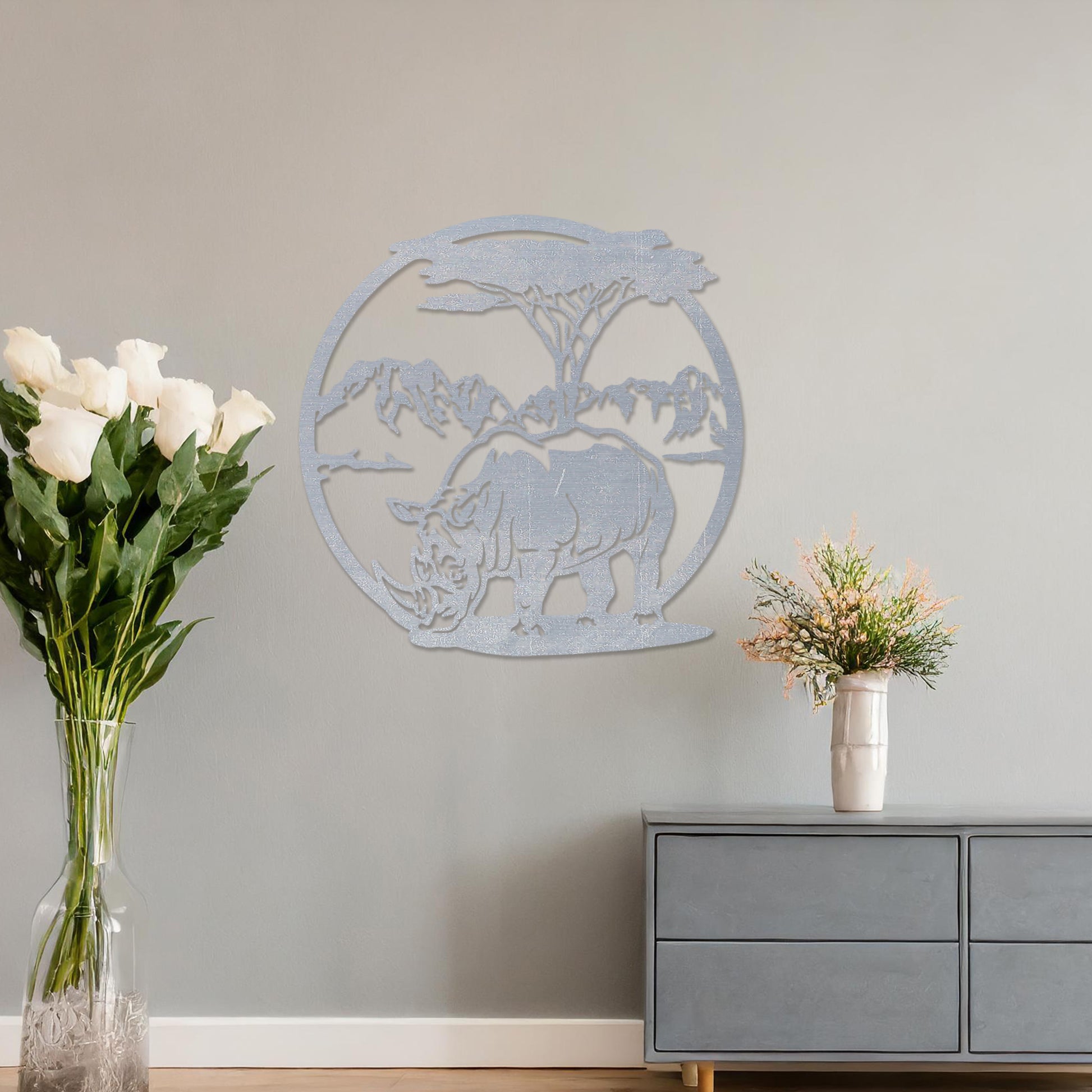 Wooden wall art design featuring a rhinoceros beneath a tree with a mountain backdrop, framed in a circular shape, placed on a neutral wall within modern room decor. The design captures the majesty of wildlife in a serene landscape.